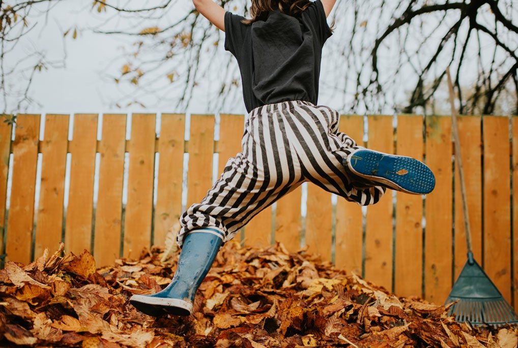 Child in striped pants and rainboots jumping into pile of leaves