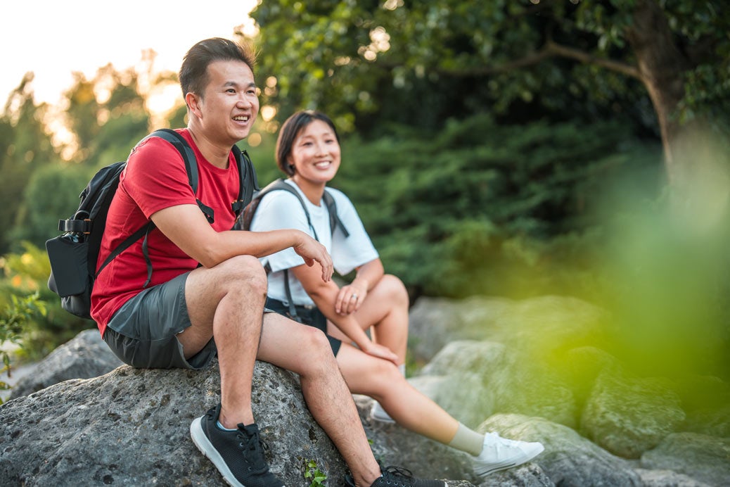 Couple with backpacks on sitting on a rock in park